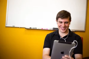 Smiling young man in a classroom with a tablet and headphones becoming proficient in a world language