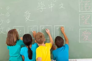 A diverse group of four young students write Chinese language characters on a chalkboard.