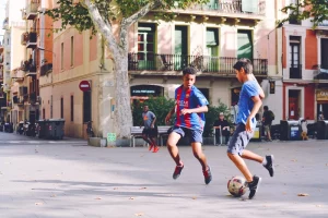 Three boys with dark complexions play soccer in a street near shops in Barcelona, Spain.