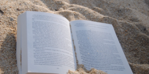 A book lies open on beach sand, written in what appears to be German.