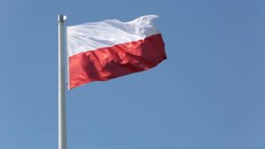 Polish flag on a pole billows high in the sky.