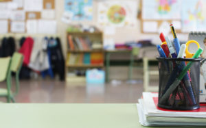 Blurred background of a colorful classroom with a pencil holder filled with pens and markers in the foreground in clear focus.